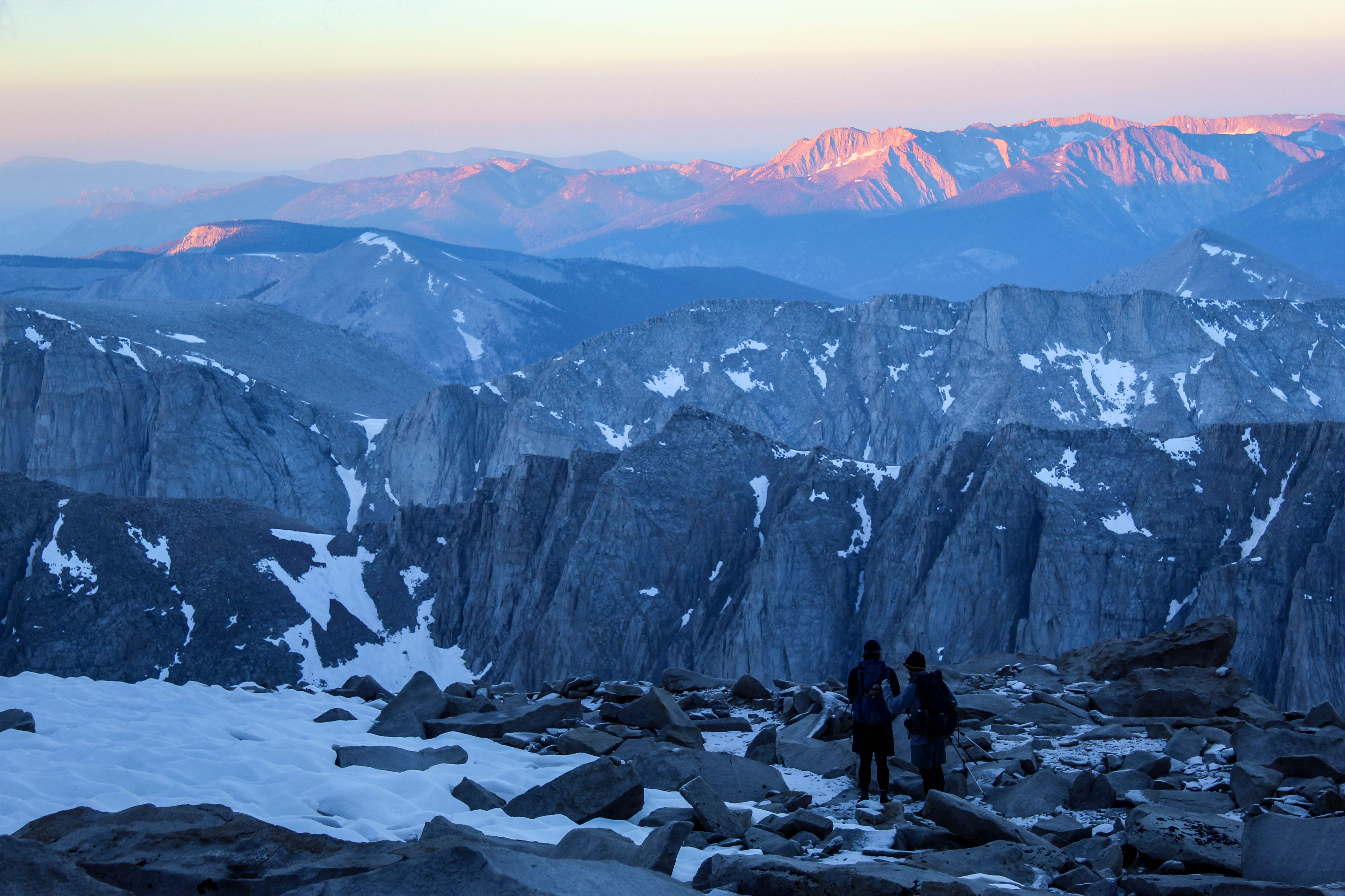 Me and a friend descend Mount Whitney as alpine glow ascends over the peaks neighboring the mountain with the first morning light.