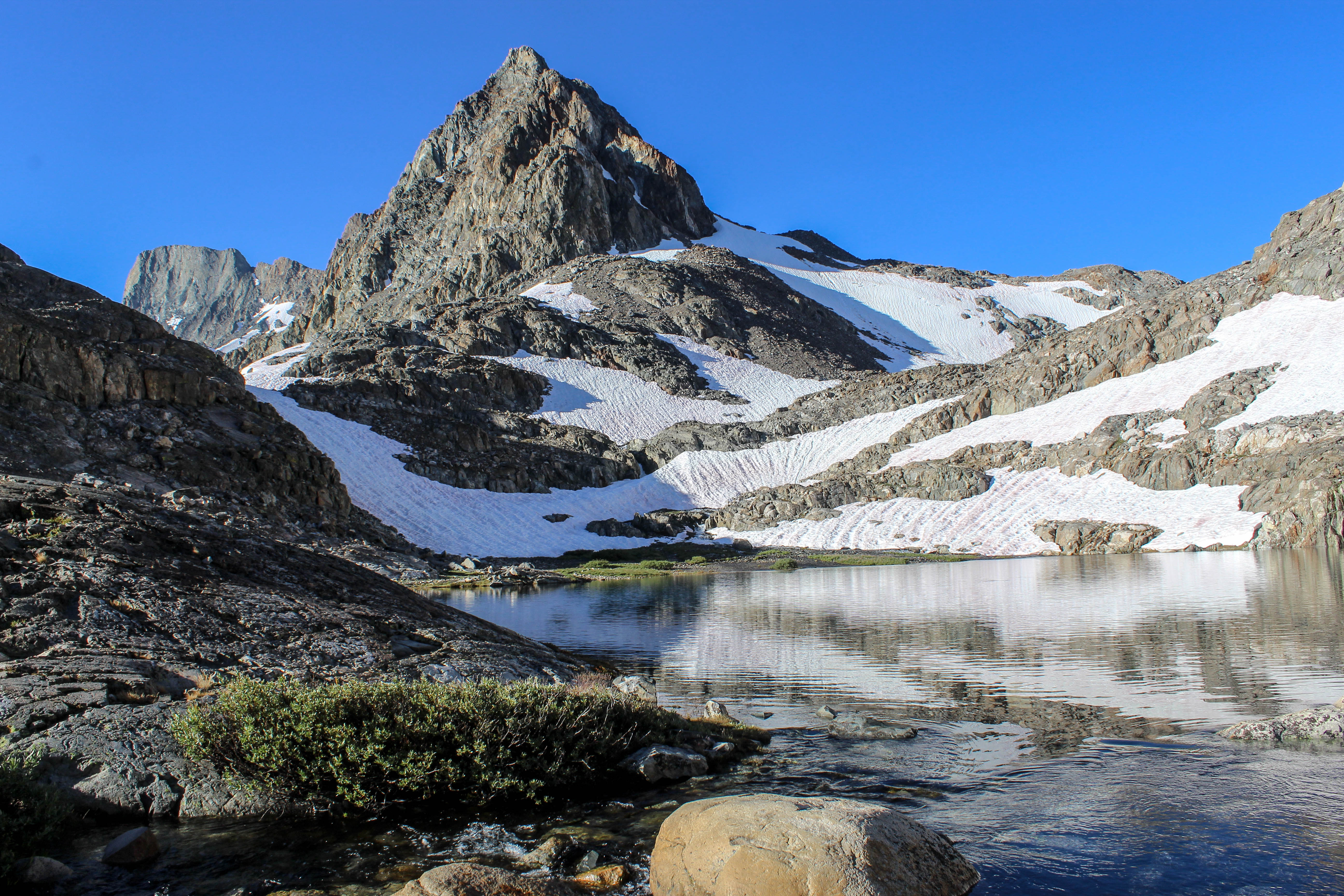 Steep snow fields scatter across the jagged peaks lying on either side of Muir Pass, melting into a deep blue, reflective lake.