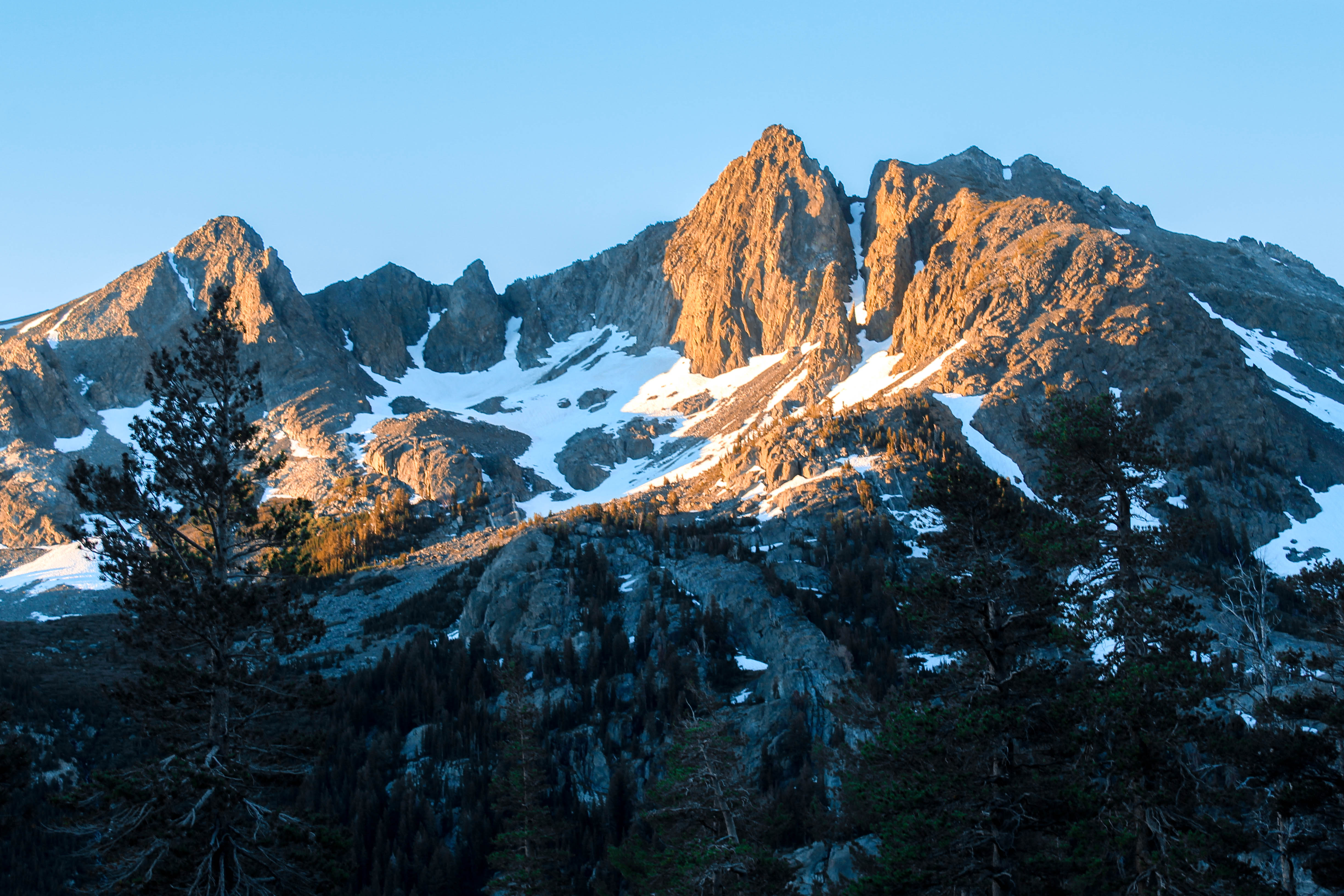 Alpine glow hangs over a bowl covered with steep snow fields and rocky outcroppings.