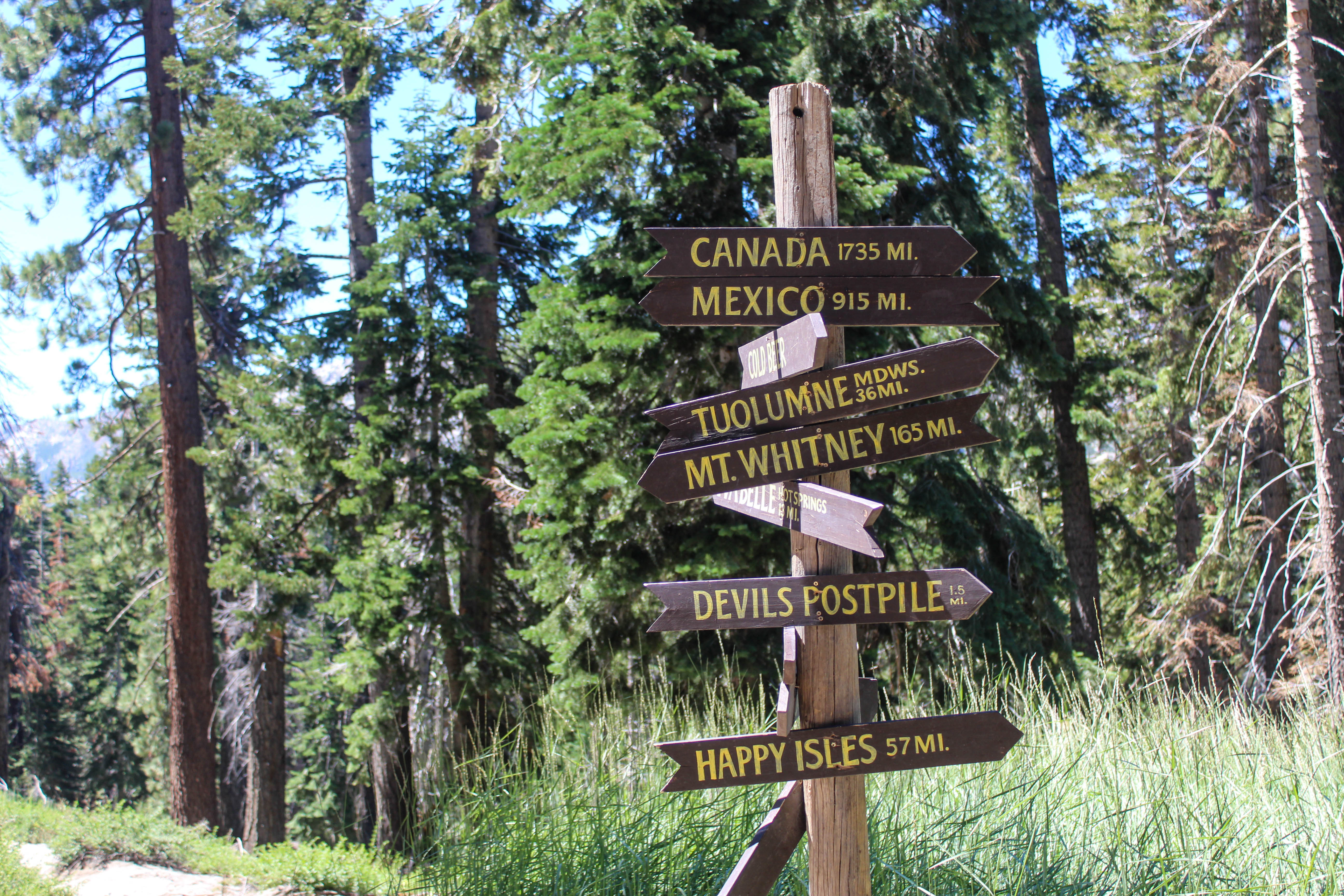 A trail junction sign with arrows pointing various ways. E.g. to Happy Isles Trailhead, Mt. Whitney, and Cold Beer.